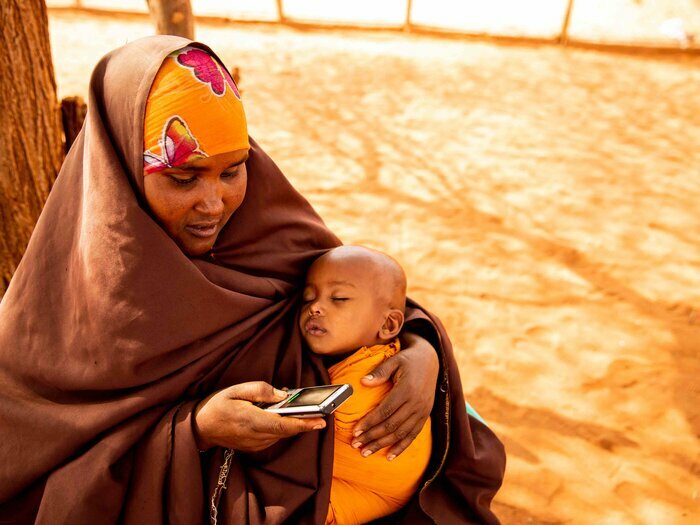 Kvinna använder en mobiltelefon, med ett barn i sin famn. 